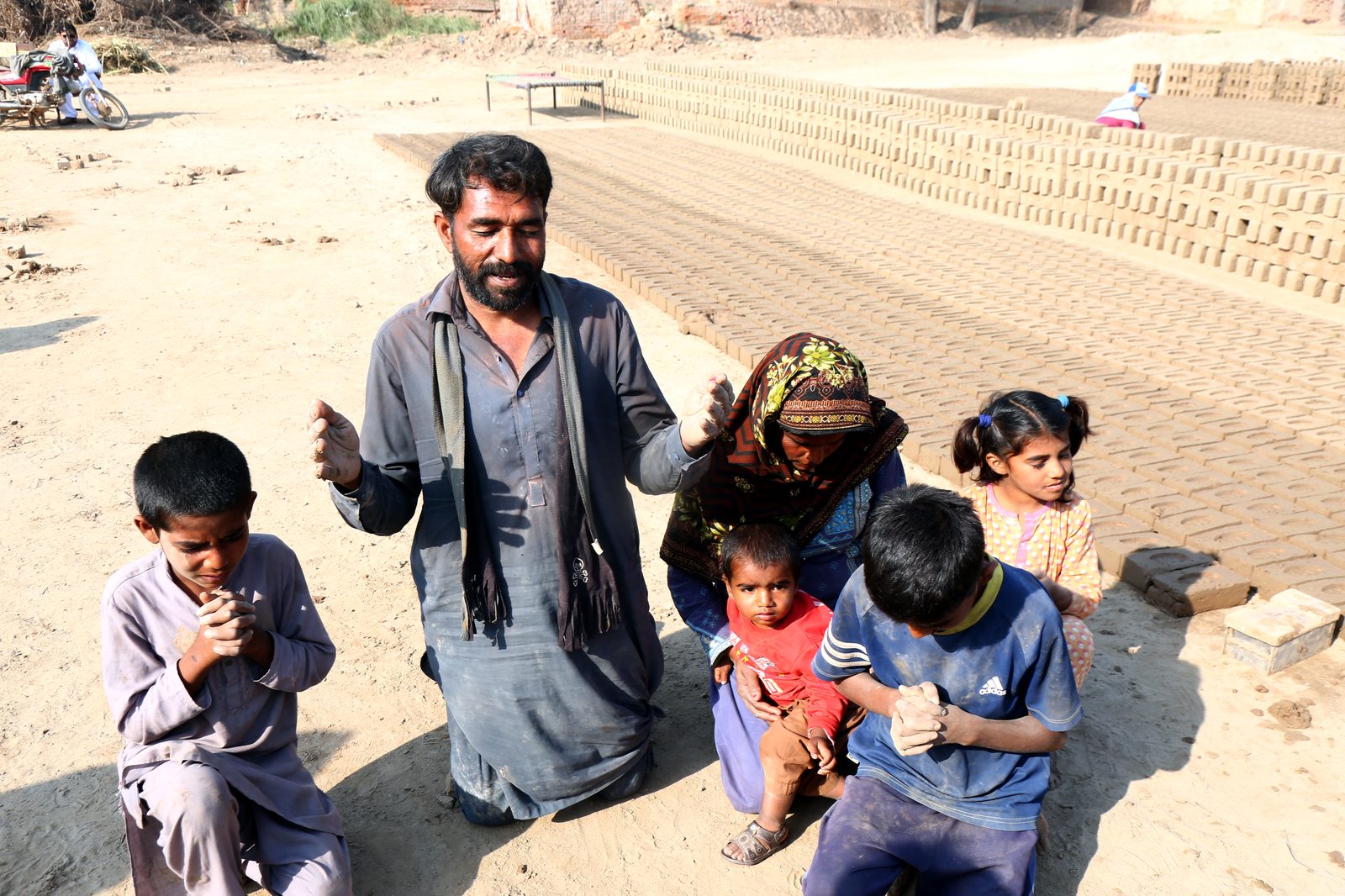 A family kneeling together in prayer at the brick kiln