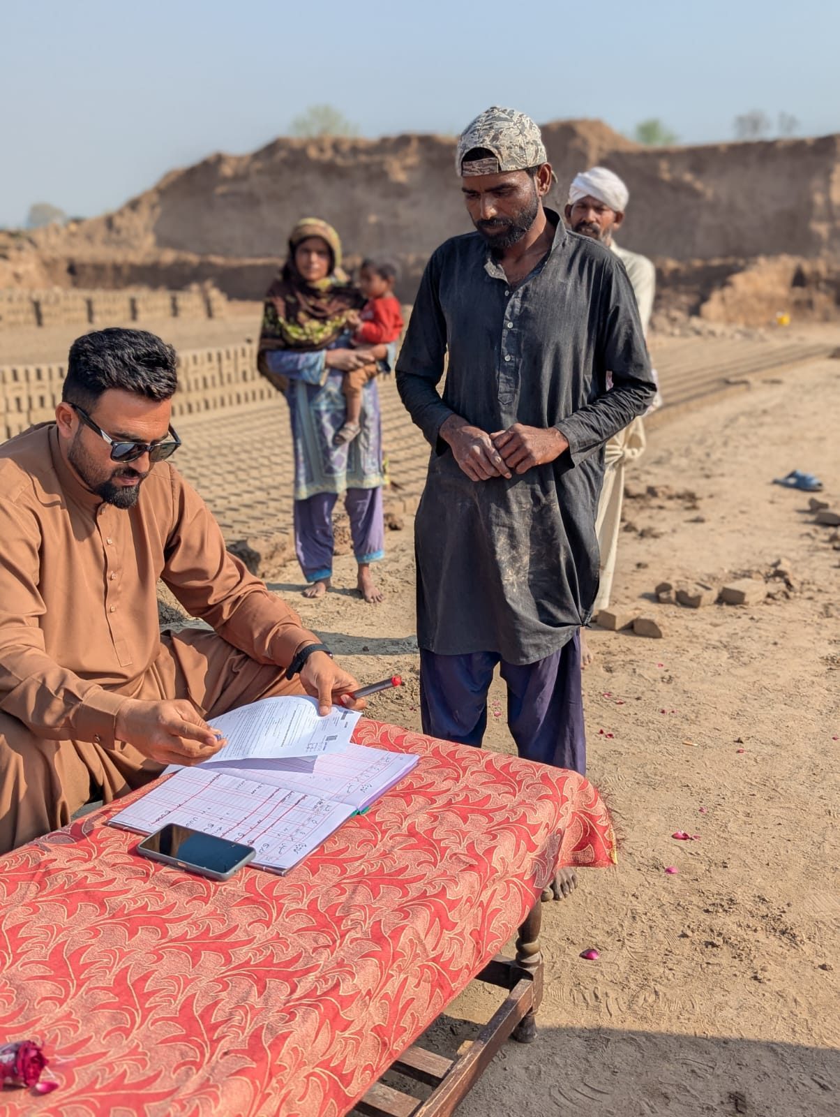 A team member reviewing the debt ledger with a family at the brick kiln