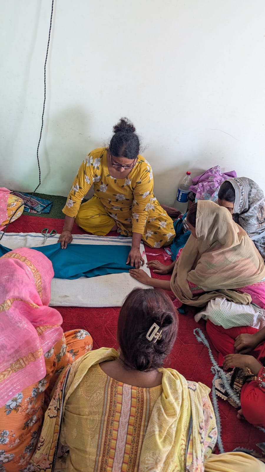 A seamstress measuring and cutting blue fabric while students look on