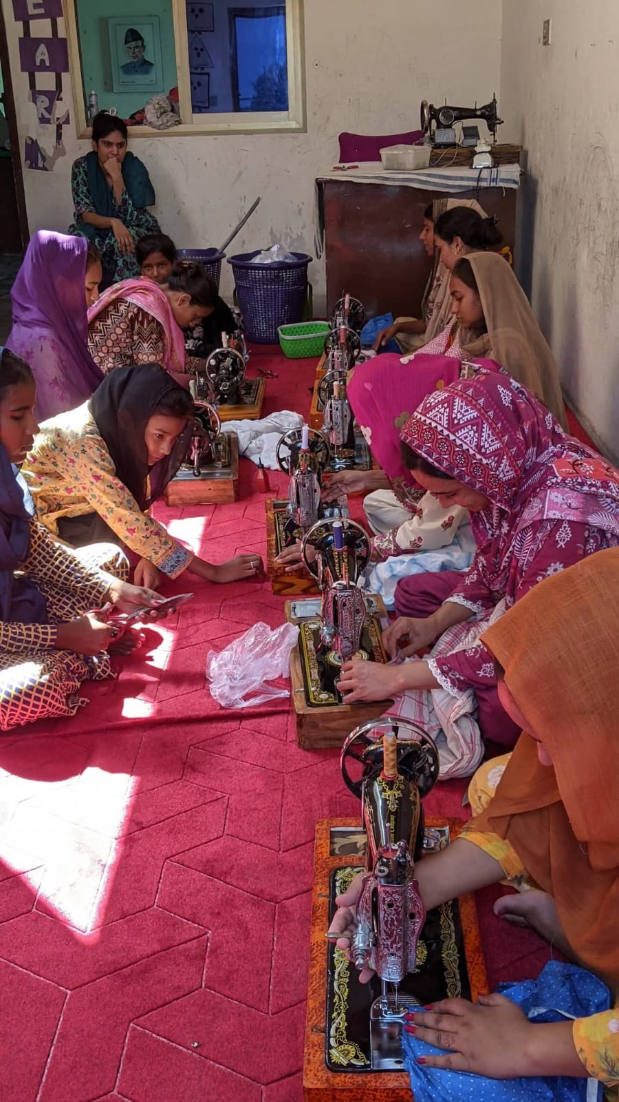 A row of girls and women seated on the floor, each working a sewing machine