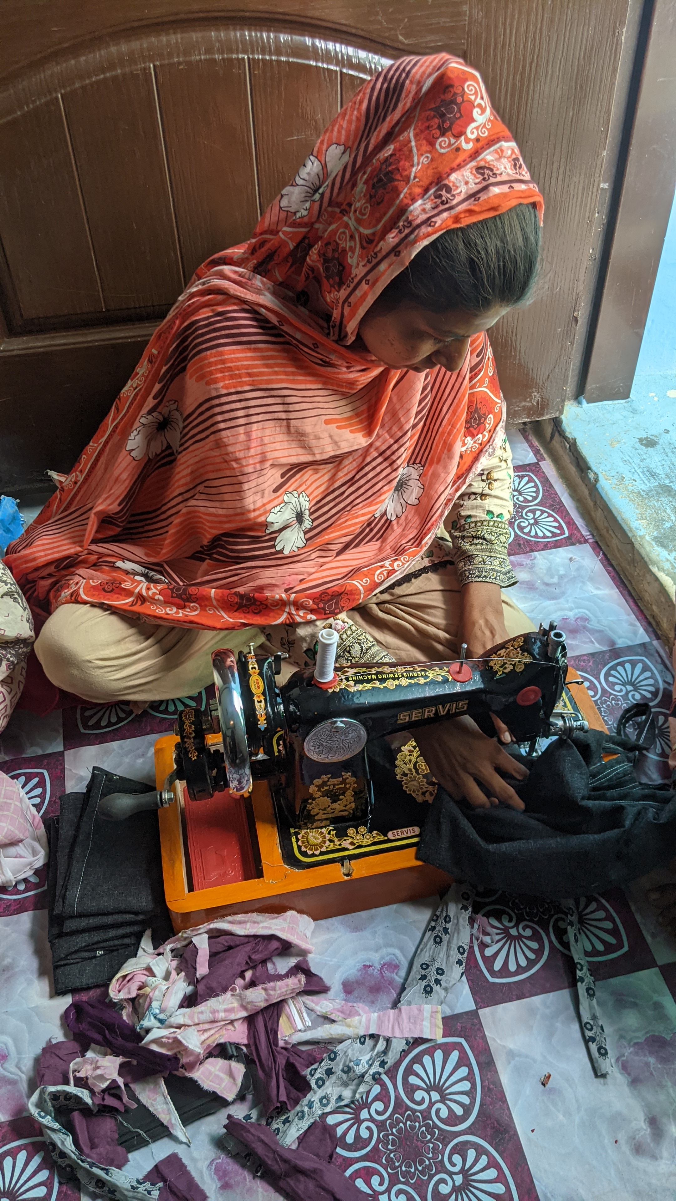A woman working a treadle sewing machine, surrounded by scraps of fabric