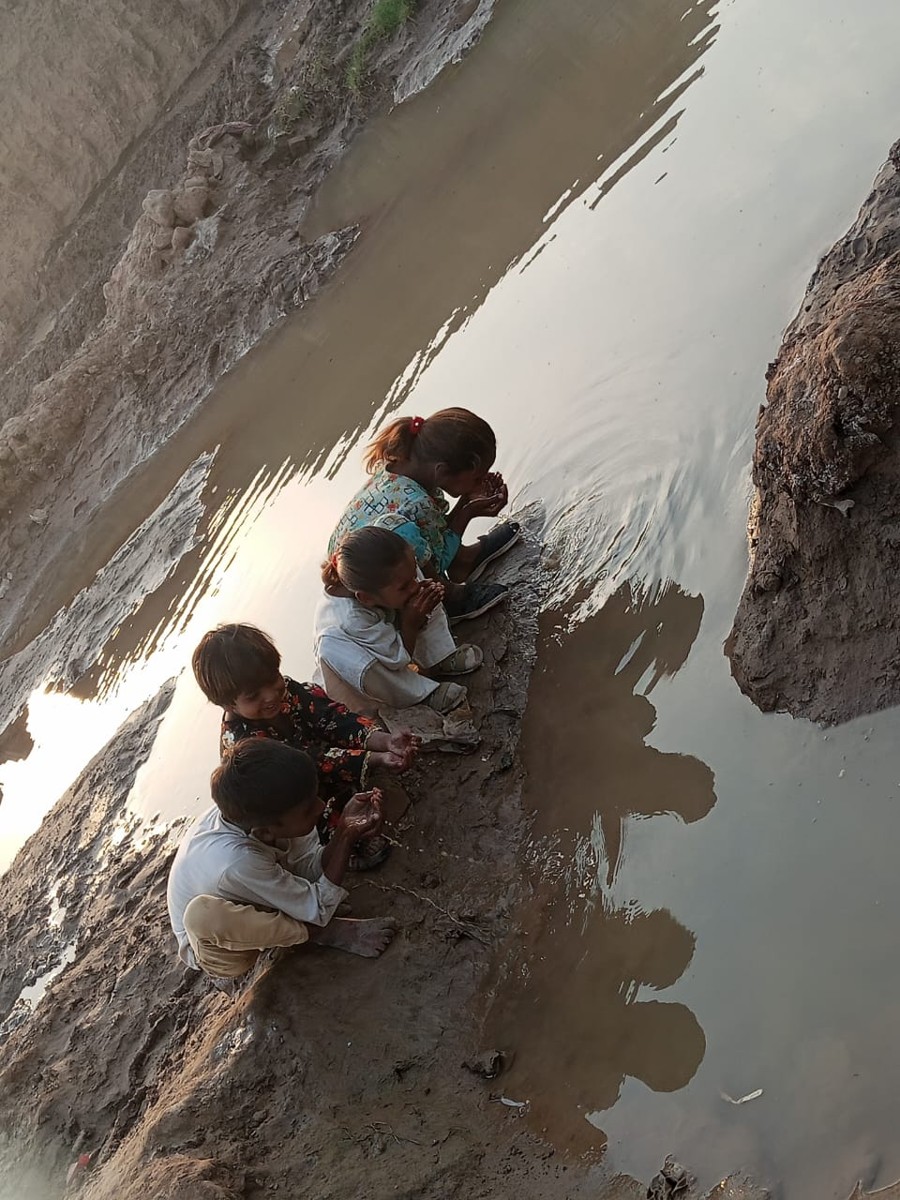 Children drinking from a muddy irrigation canal before the well was built