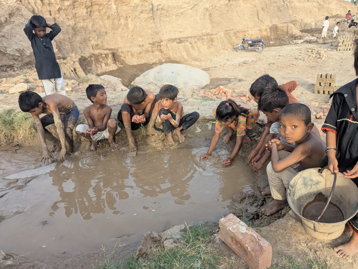 A group of children washing and drinking from a muddy water pit near the brick kiln
