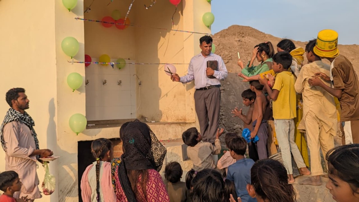 Pastor Shahid Naveed cutting the ribbon at the new clean water station, surrounded by children
